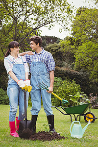 年轻夫妇手持铲子和堆肥叉手套消遣花园喷壶环境农业服装栽培工装裤园艺背景图片