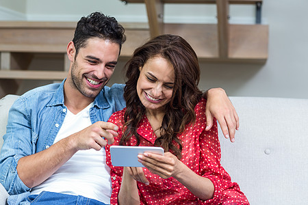 使用智能手机微笑的情侣住所休闲沙发女士公寓夫妻幸福技术男性家庭生活图片