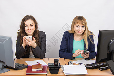 两名办公室雇员在办公桌上从事个人移动电话业务 负责私人事务图片