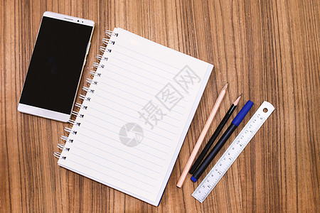 木桌上带铅笔笔和智能手机的空白笔记本框架文档学校白色建造笔记组织床单软垫商业图片