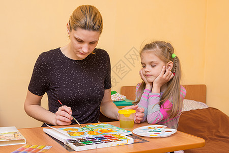 一个小女孩正在仔细观察 一位老师 他教如何画水彩色图片
