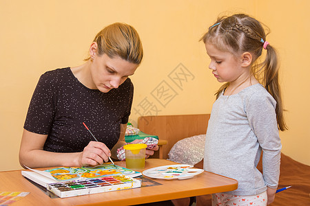 小女孩看着画家在桌边的纸上涂水彩色图片