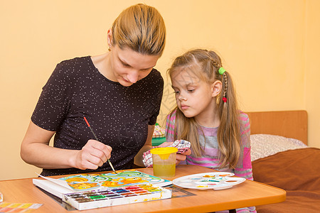 女孩艺术家教一个坐在桌边的小女孩 在纸上画水彩图片