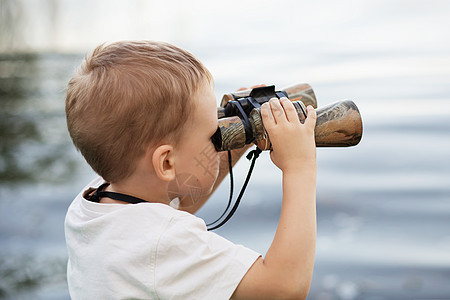 小男孩在河岸看望双筒望远镜码头孩子们游客机械支撑海岸手表流浪者男生喜悦图片