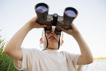 小男孩在河岸看望双筒望远镜孩子们孩子情感游客喜悦眼镜探险家男生流浪者手表图片