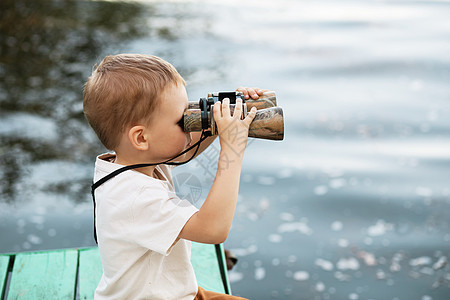 小男孩在河岸看望双筒望远镜池塘眼镜孩子们快乐游客微笑机械流浪者童年支撑图片