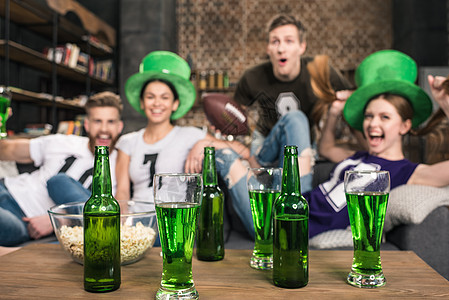 喝着瓶装绿啤酒和杯子的绿色啤酒 在朋友庆祝节日附近图片
