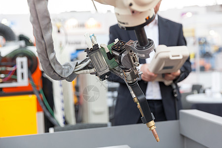 工业焊接机器人机械臂 背景中模糊的操作员图片