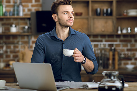 带着咖啡杯 拿着笔记本电脑坐在桌上的青年男子图片