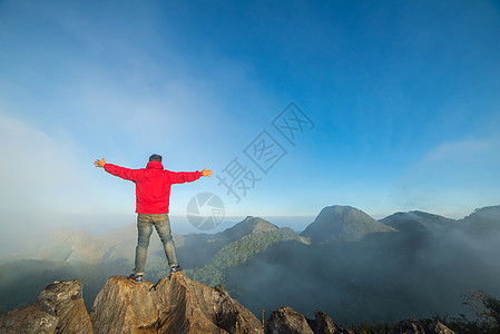 在山顶上的人坐在岩石上 看着风景的土地顶峰冒险远足者生活旅行薄雾山脉背包享受天空图片