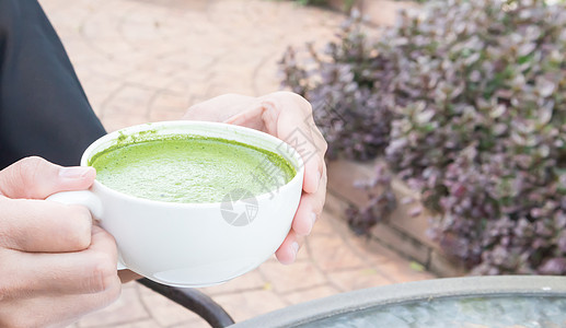 女士手握着一杯热火辣的拿铁或绿色茶木头奶油粉末杯子牛奶食物味道女孩泡沫艺术图片