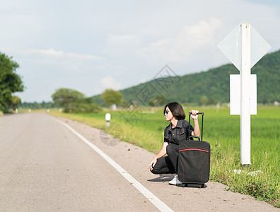 车载记录仪在公路上搭便车载行李的妇女旅行青少年短发女士游客太阳镜女孩牛仔裤旅游远足背景