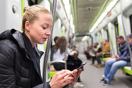 年轻女孩在地铁的手机屏幕上阅读日程乘客过境民众旅行铁路通勤者女性航程城市图片