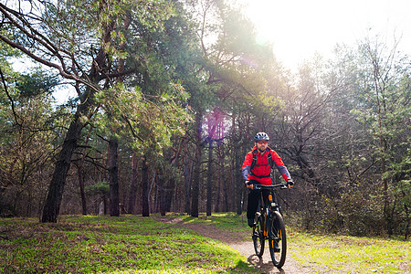 赛车手骑着山上摩托 在阳光下美丽的松林的轨迹上 冒险和旅行概念太阳安全男人头盔车轮男性松树魔法运动员射线图片