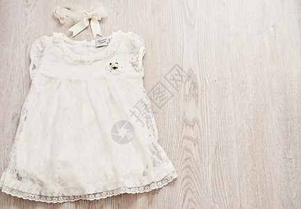 浅灰色木制背景上的复古婴儿白色蕾丝连衣裙和蝴蝶结头带 顶视图 复制空间图片
