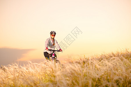 年轻女子在日落 冒险和旅行的青春草原上骑着山地自行车跑山地车羽毛女士场地女性车轮地平线行动运动头盔图片