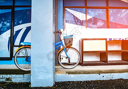 双轮车靠在木制鞋架旁的一根杆子上 放在一栋有照明灯的大楼水泥地板上自行车街道篮子倾斜运输耀斑金属木头车辆车轮图片