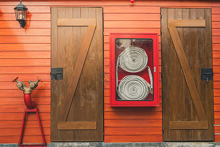 橙色木墙上挂着的红色橱柜中的消防水龙带 用于安全和保障系统的消防应急设备箱 消防安全泵 消防系统的雨淋系统 管道防火图片
