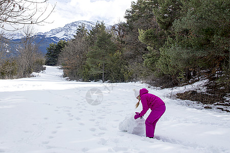 穿着明亮冬衣的年轻女子 在森林里做雪人图片