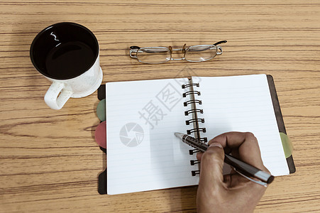 写在他的日记的商务人士 在木桌上的咖啡和眼镜旁边打开带有空白页的笔记本 商业静物概念与桌上的办公用品 带复制空间的顶视图部位过程图片