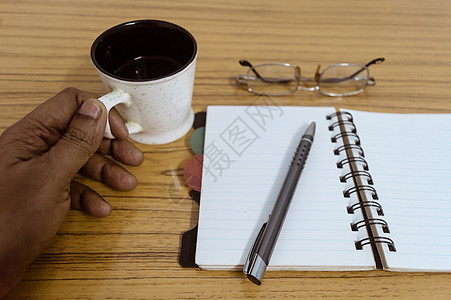 商务人士拿着一杯咖啡 带有眼镜和笔的商务口袋规划师准备好记录约会 商业静物概念与桌上的办公用品 准备好样机的空白页图片