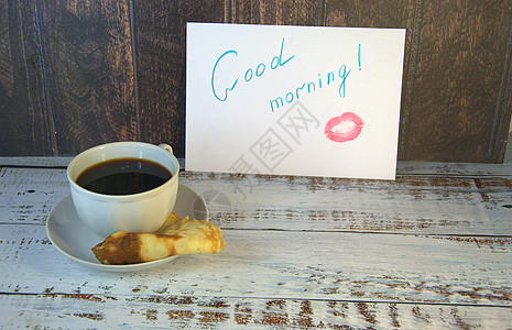 咖啡海报茶碟上的一杯咖啡 新鲜出炉的煎饼和一张写着早安心愿并涂了一丝口红的纸桌子飞碟陶瓷早餐杯子愿望海报厨房金子恋爱背景