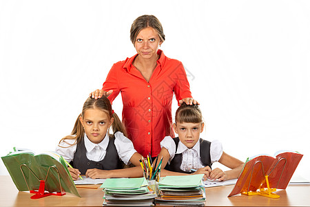 孩子生气愤怒的老师站在坐在她办公桌前的学生后面 把手放在孩子头上 (笑声)背景