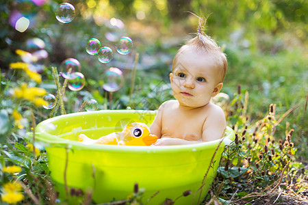 盆子里的托德勒男孩 用泡泡和鸭玩具洗澡喜悦身体太阳婴儿享受绿色孩子黄色小鸭子橡皮图片