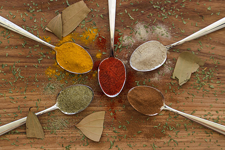 在勺子上安排各种彩色调味品厨房辣椒香菜草本植物金属粉末肉桂桌子香料木头图片