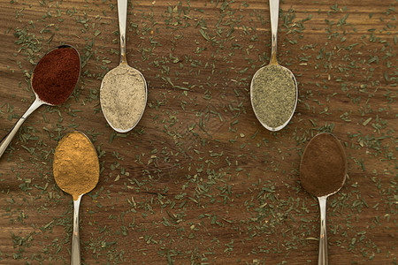 在勺子上安排各种彩色调味品厨房草本植物芳香辣椒桌子金属粉末木头种子香气图片