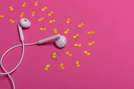 粉红色背景上的白色耳机和黄色纸币 从上面看粉色配饰耳朵工作室文化笔记电话金属娱乐电子图片