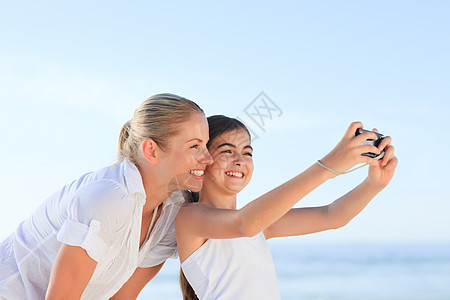 小女孩给自己和妈妈照一张相的小孩相机微笑旅行袖珍母亲假期摄影女士海滩拥抱图片