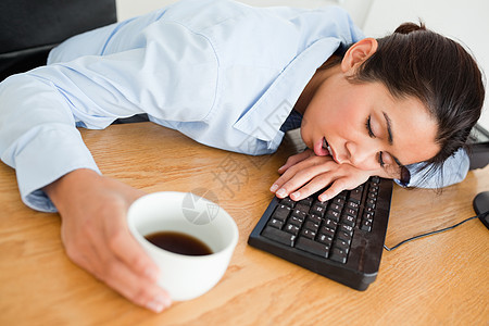 迷人的女人睡在键盘上 同时端着一杯咖啡背景图片