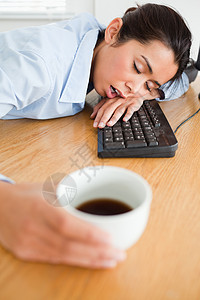 美丽的女人睡在键盘上 同时端着一杯咖啡背景图片