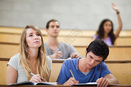同学举手时 学生在写笔记的同时拉起她的手高清图片