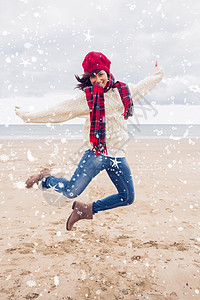 在海滩上跳跃的时尚温暖衣着中 女性综合形象帽子活力针织帽衣物身体微笑牛仔裤牛仔布海岸线靴子图片