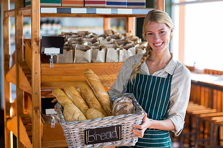 在面包柜台上拿着一篮子面包的微笑的女性工作人员售货员工人职员护理围裙购物者卫生快乐店铺生活方式图片