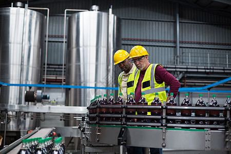 工厂工人在饮料生产厂监控冷饮瓶制造业检查防护男人男性瓶子技术喜悦安全帽同事图片