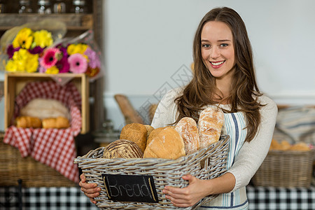 在柜台拿着一篮袋式面包包的微笑的女性工作人员肖像快乐烘焙零售商包子诱惑职员面包围裙喜悦女士图片