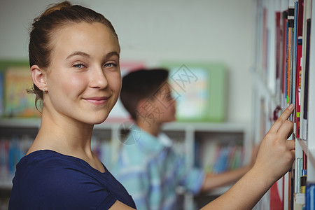 从学校图书馆图书架上挑选书本的女学生孩子快乐金发女郎书架女性学生休闲男性文学智慧图片