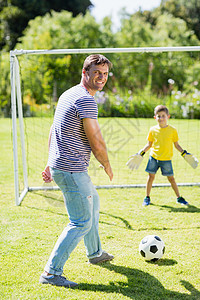 父亲和儿子在公园踢橄榄球足球乐趣花园闲暇孩子服装门柱休闲草地晴天图片