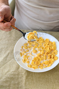 一个剪短的男人拿着一把勺子 勺子放在玉米片里 牛奶放在普通的粗糙桌布上的白盘子里 从上面看 概念 简单快速的美式健康早餐奶制品生图片