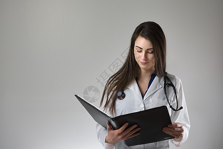 女性保健专业检查员在灰色背景上孤立的病人病历表 颈部围着止步镜 穿白色外套并扣上锁护士手臂照顾者卫生练习药品压力老年助理医师图片