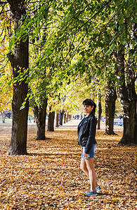 在公园散步时笑着女人的年轻黑发女孩季节毛衣裙子闲暇晴天女性森林阳光太阳城市图片