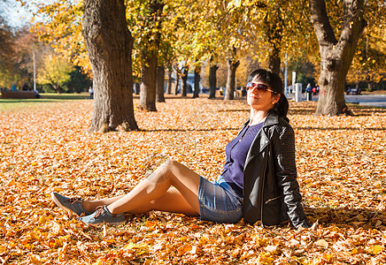 秋天坐在公园的草地上的年轻女子城市裙子季节女性晴天头发阳光太阳镜闲暇黑发图片