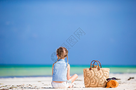 沙滩小女孩在暑假期间带沙滩袋和毛巾的可爱小女孩游客旅行海岸线假期太阳镜微笑海滩旅游玩具海岸背景