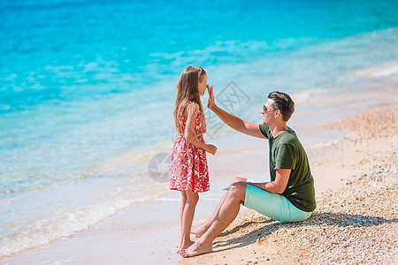 父亲在热带海滩对女儿施防晒霜 在热带海滩施用保护奶油预防皮肤父母日光浴享受太阳镜太阳孩子婴儿海洋图片