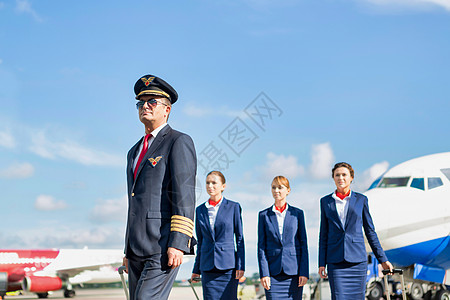 与三名年轻的美丽空服员在机场对着飞机行走的成熟飞行员肖像 该机旅行下载飞机场木板服务员职业工作服务畅销书队长图片