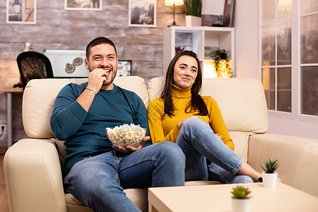 在家吃流行玉米和看电视的一对英俊夫妇喜悦乐趣闲暇房间爆米花微笑快乐休息女士电视图片