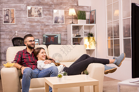 美丽的年轻夫妇在沙发上放松 同时观看电视上的电影程序夫妻长椅娱乐房子房间恋人女士专注公寓背景